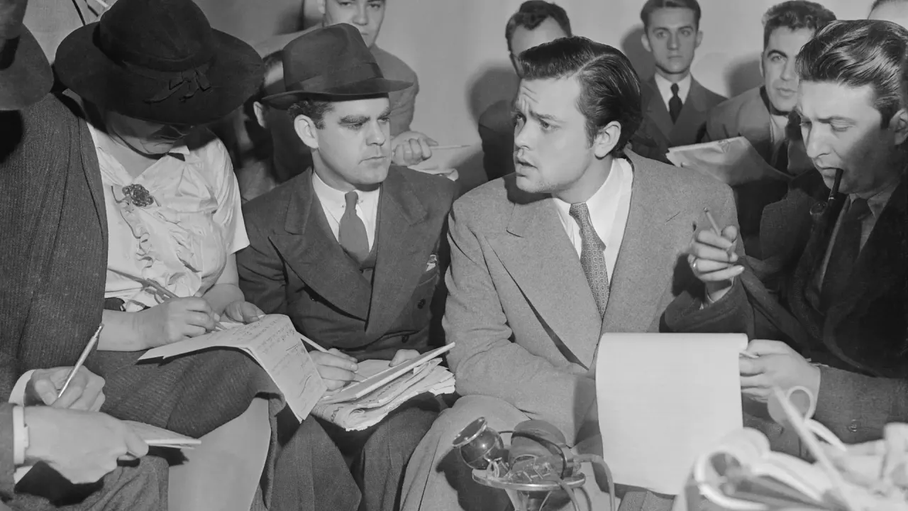 Orson Welles sidder tæt omgivet af journalister med notesblokke og mikrofoner den 31. oktober 1938.
