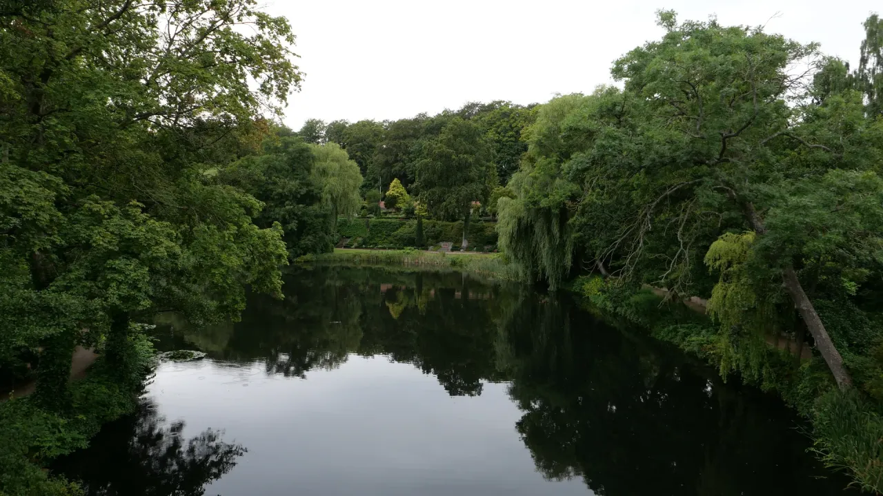 Kirkegårdssøen ved Humlebæk med træer, stejle grønne skråninger og gravsteder langs bredden.