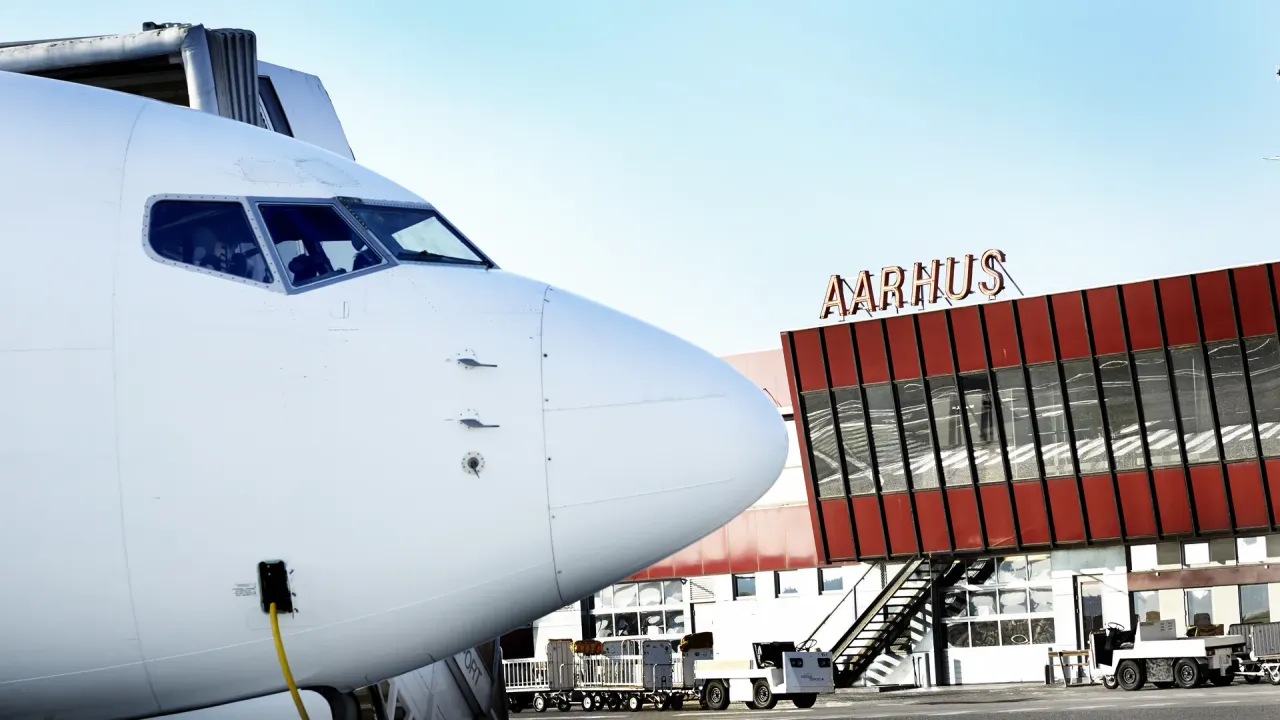 Næsen på et passagerfly foran Aarhus Airports røde terminalbygning.