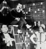 En komisk filmscene fra 1925 med tre personer foran store krydsord på væggene.
