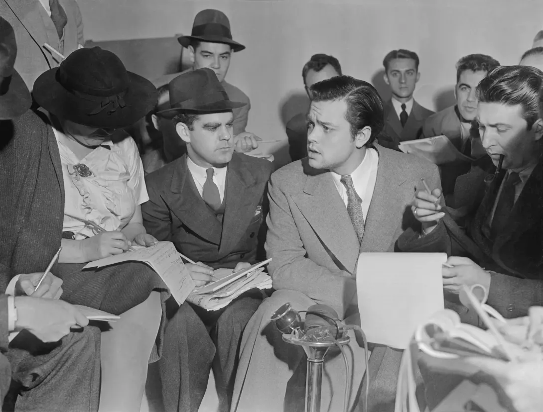 Orson Welles sidder tæt omgivet af journalister med notesblokke og mikrofoner den 31. oktober 1938.