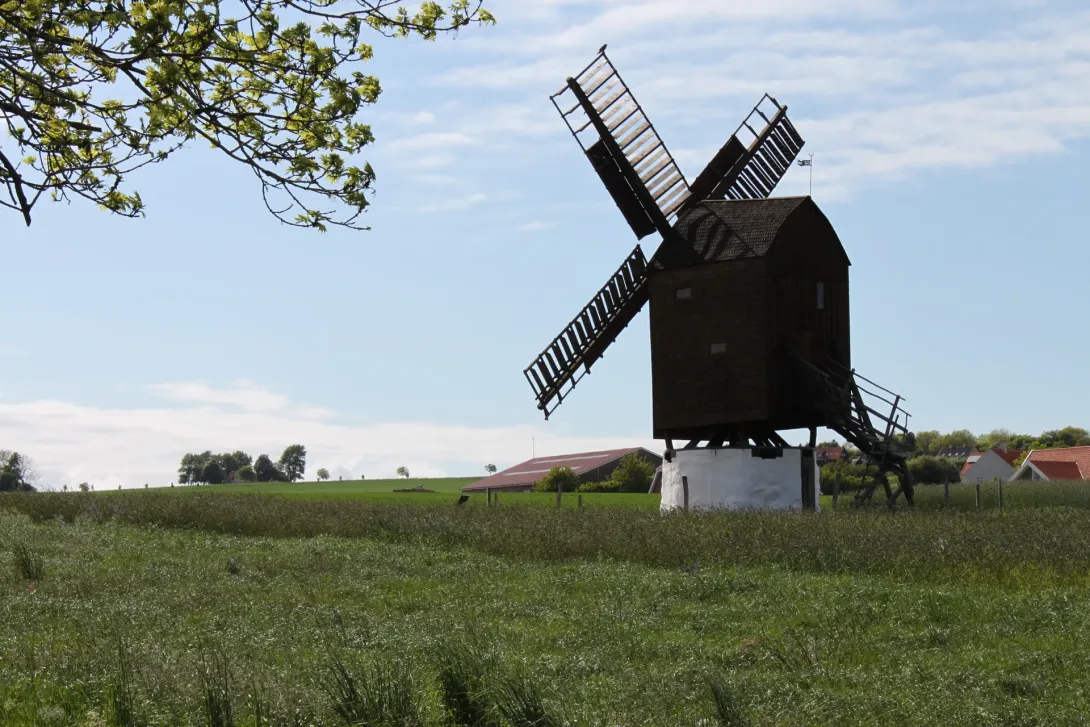 Melsted stubmølle på Bornholm med mørk træbygning og vinger over en grøn mark.