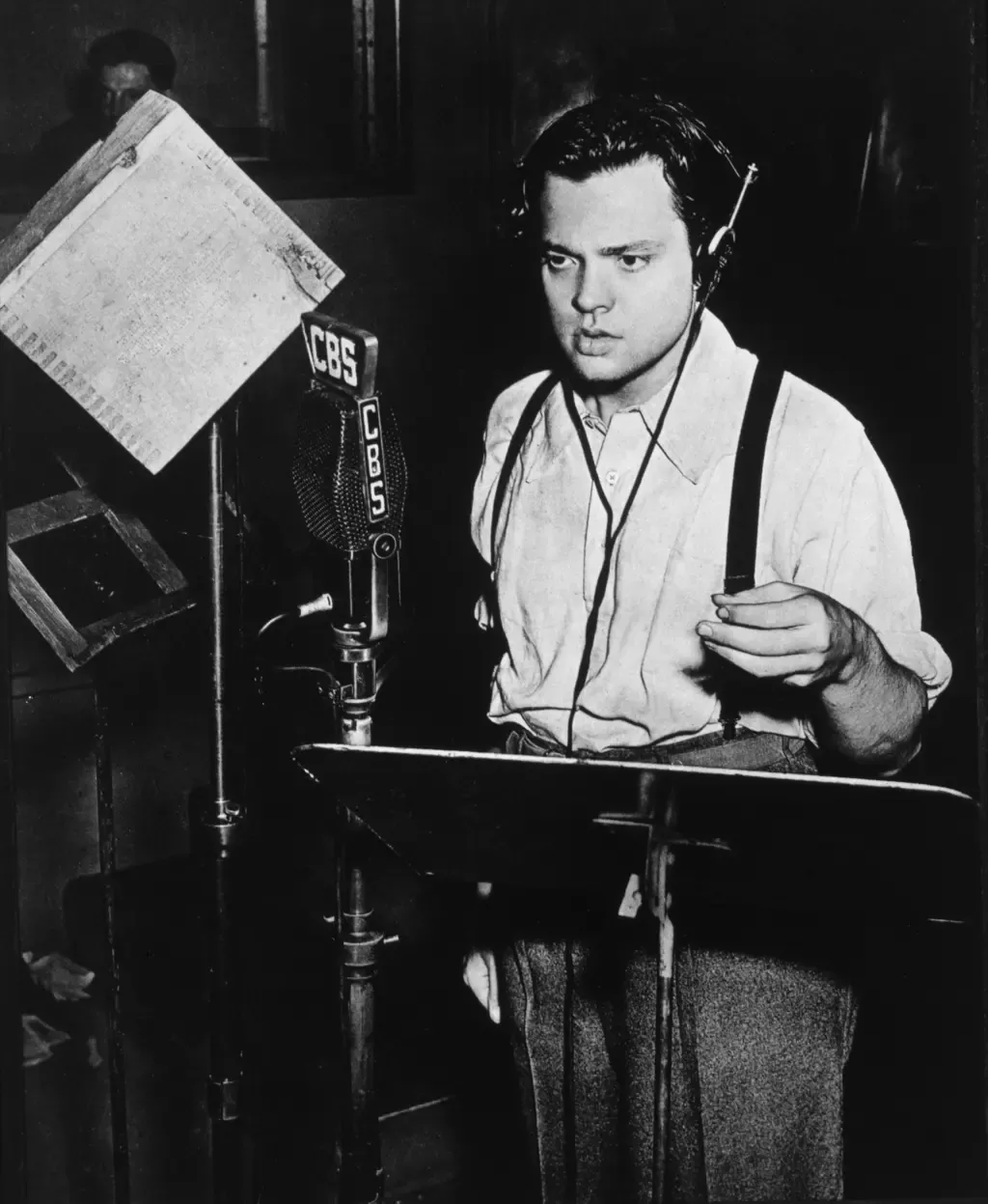 Orson Welles med hovedtelefoner og manuskript foran en CBS-mikrofon i radiostudiet i 1938.