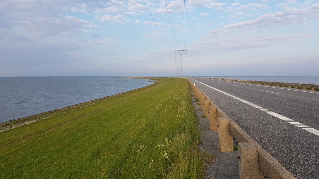 Vejen på Rømødæmningen med græsbevokset skråning og vand på begge sider.