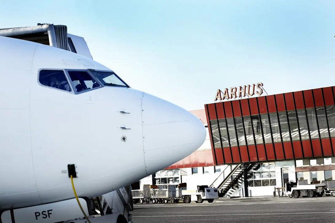 Næsen på et passagerfly foran Aarhus Airports røde terminalbygning.