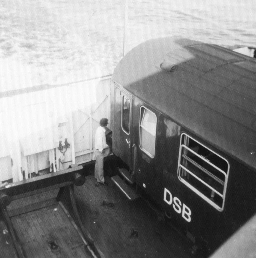 En mørk DSB-personvogn står på jernbanespor om bord på en Storebæltsfærge i 1976.