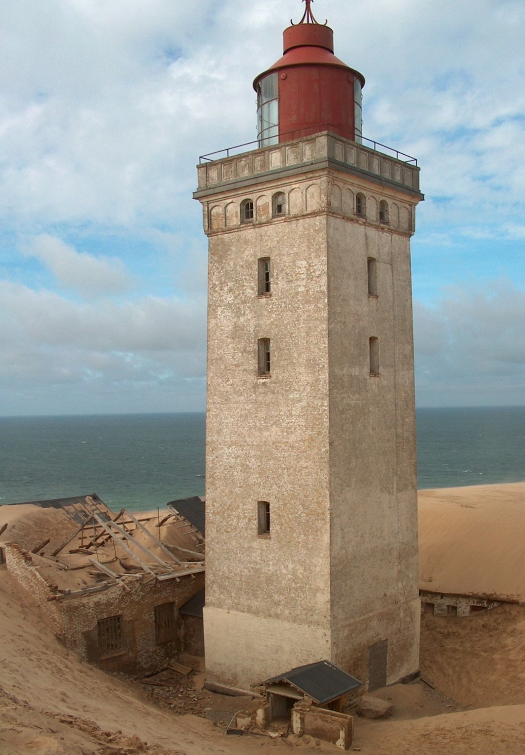 Rubjerg Knude Fyr med sand og delvist begravede bygninger omkring tårnet.